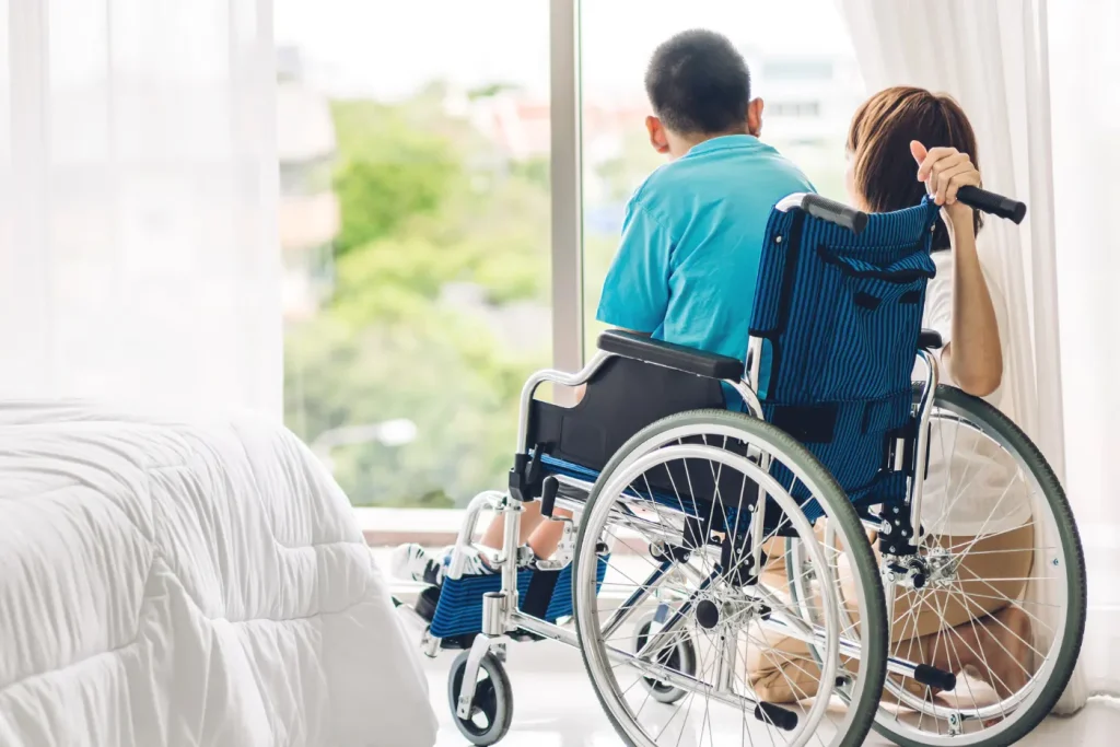 Disabled man in wheelchair looking out window with support worker