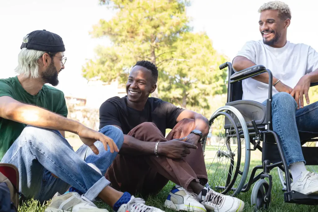 Three friends, one disabled in wheelchair, talking in park