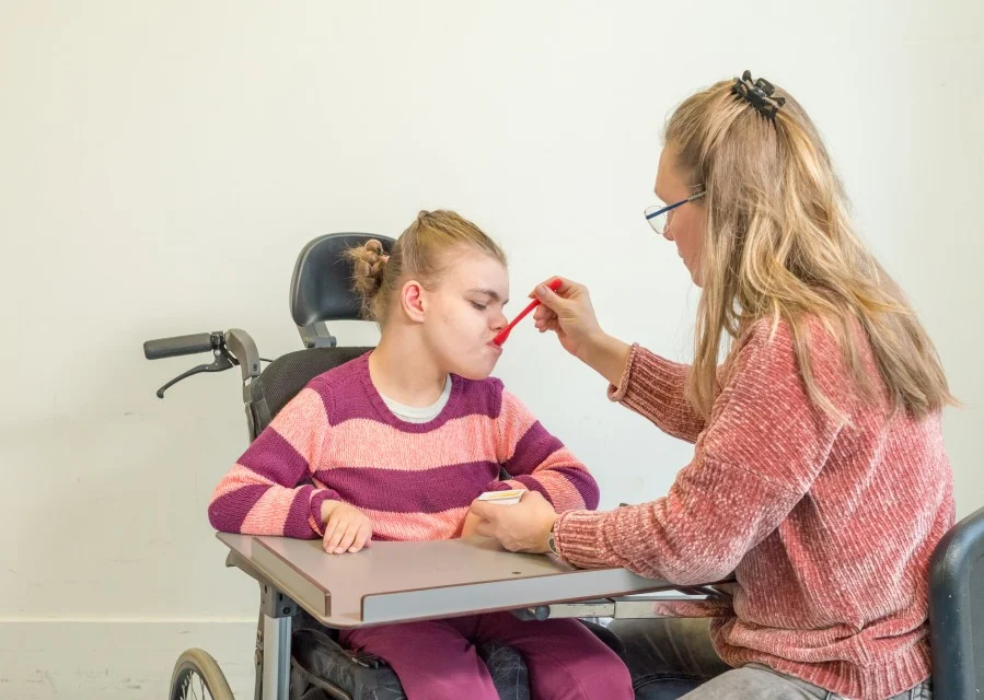 Support worker feeding disabled girl in wheelchair