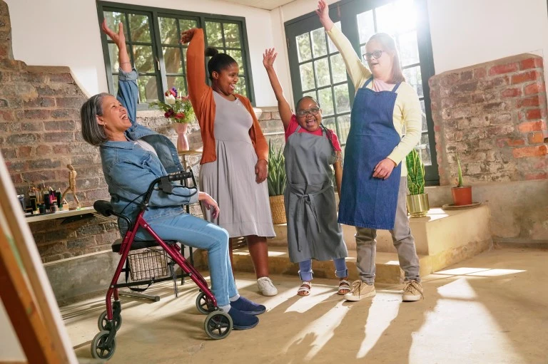 Four disabled friends smiling with hands in the air